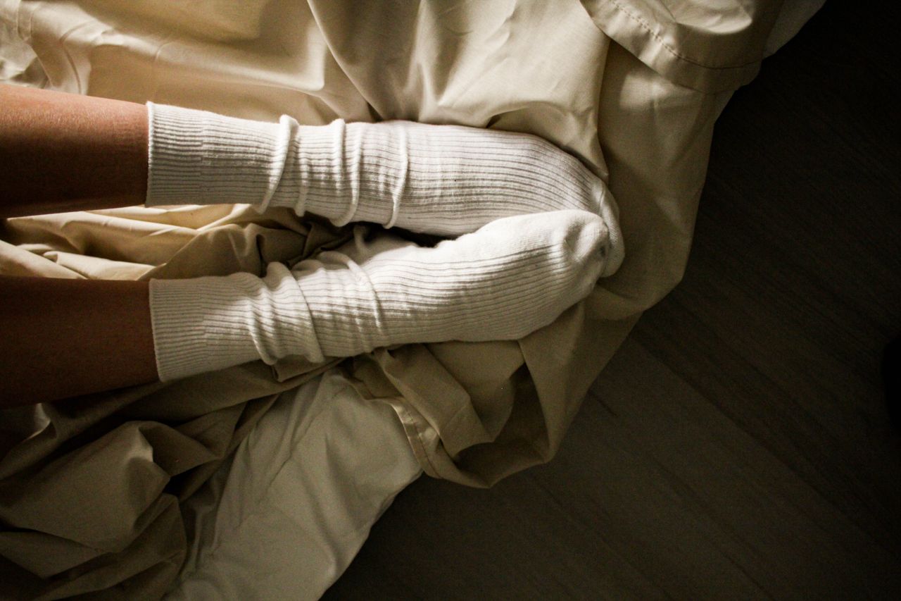 Comfortable legs in warm white socks resting on a bed with soft sheets.