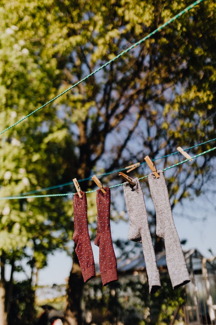 about-us Various colors socks hanging on ropes with clothespins against green branches of tree in sunny weather