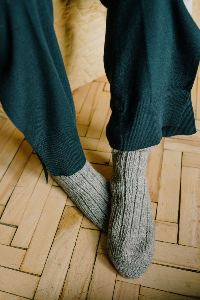 who-we-are Woolen knitted socks over black pants on a wooden parquet floor.