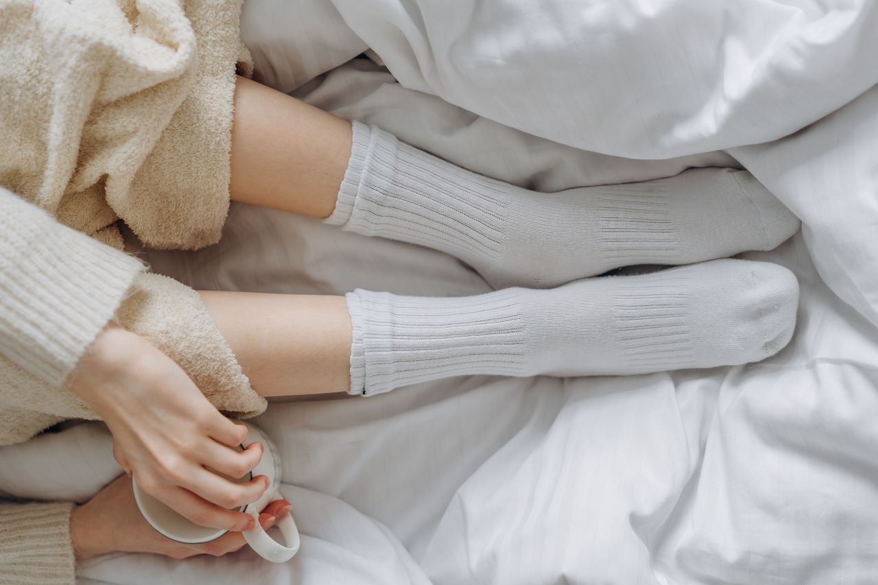 our-story Relaxing indoors wrapped in white linens and warm clothing, enjoying a soothing moment with a cup.